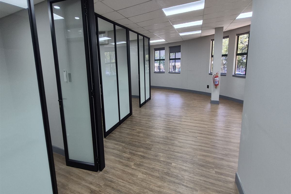 Modern open-plan office space featuring glass partition walls, wood-look vinyl flooring, and recessed ceiling lighting, providing a bright and professional work environment.