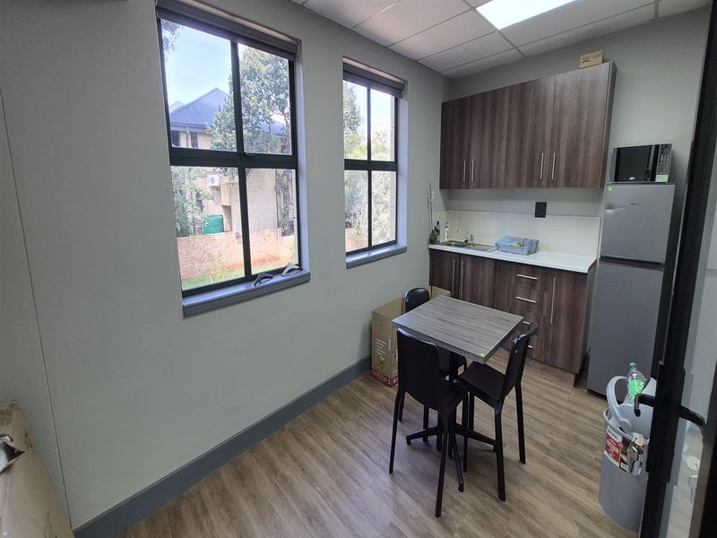 A compact office kitchenette featuring modern laminate cabinetry, wood-look flooring, and a functional sink area with a tiled backsplash.