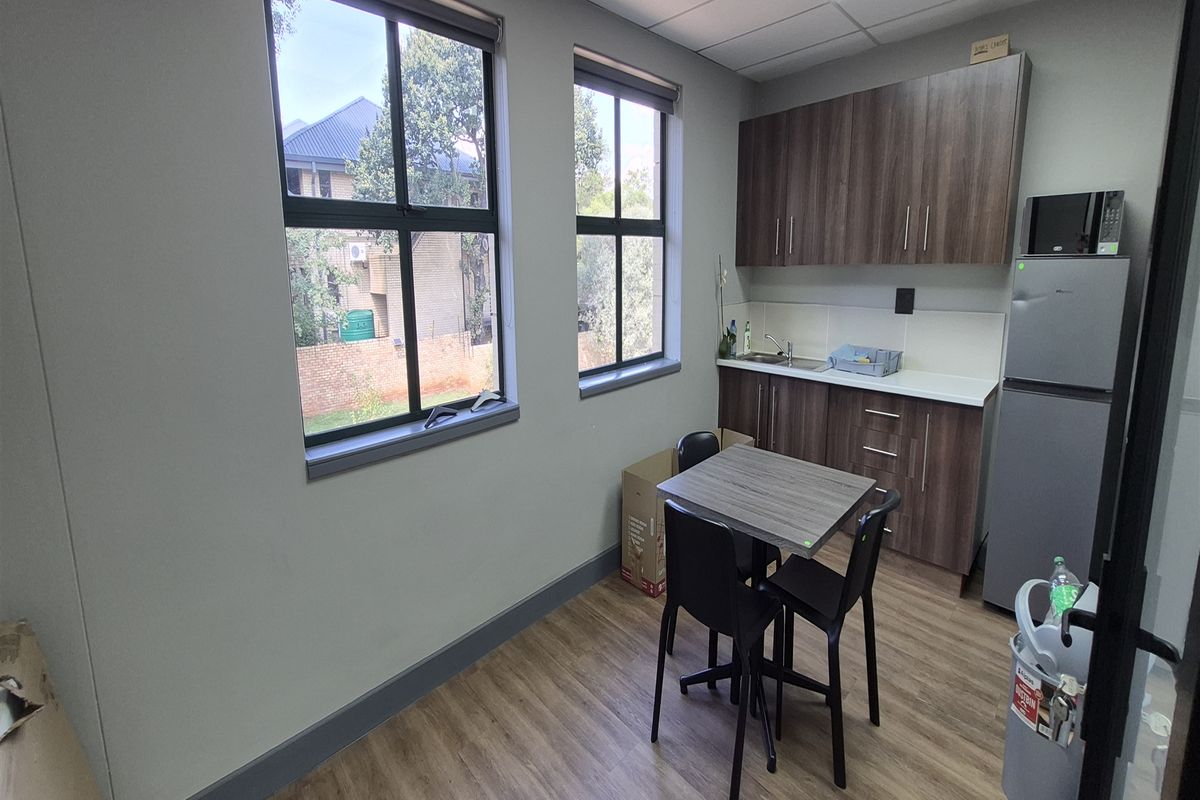 A compact office kitchenette featuring modern laminate cabinetry, wood-look flooring, and a functional sink area with a tiled backsplash.