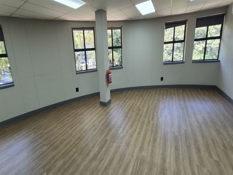 A bright, empty office space featuring modern laminate flooring, suspended ceiling with recessed lighting, and large windows providing natural light.