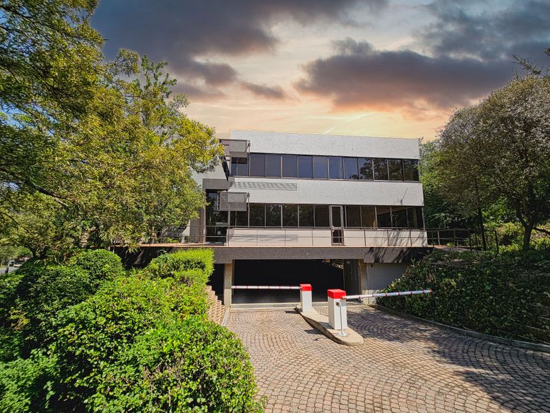 Front view of a professional office building featuring a secure boom gate entrance, cobblestone driveway, and underground parking access.