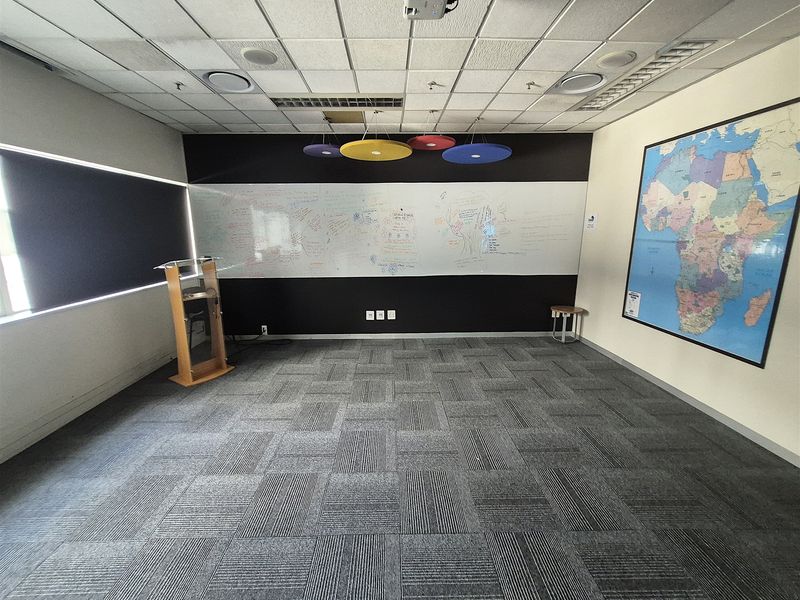 A functional office space featuring carpet tiles, a large whiteboard wall, suspended ceiling with integrated projector, and recessed lighting.
