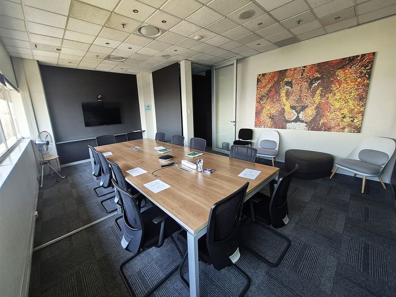 A professional office boardroom featuring a large meeting table, suspended ceiling with recessed lighting, and durable carpet tiles.