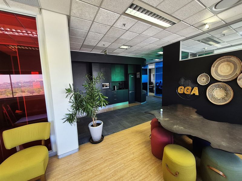 Modern office space featuring a combination of laminate and carpet flooring, a built-in kitchenette, and a contemporary open-plan layout with glass partitions.