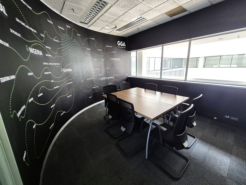 A professional office meeting room featuring a curved feature wall with a map graphic, large windows, suspended ceiling, and carpeted flooring.