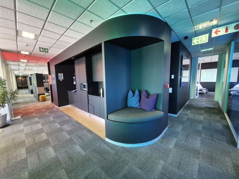 Modern office corridor featuring a built-in kitchenette and integrated seating nook with contemporary finishes and professional lighting.
