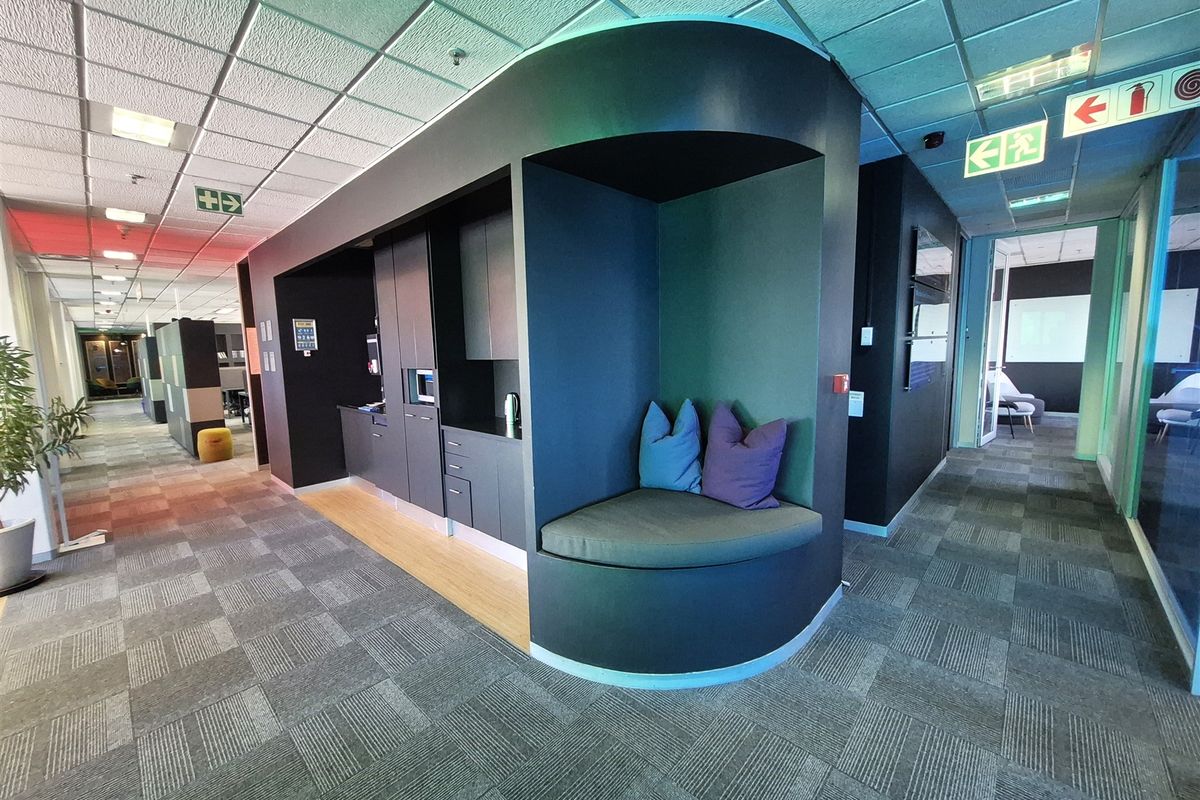 Modern office corridor featuring a built-in kitchenette and integrated seating nook with contemporary finishes and professional lighting.
