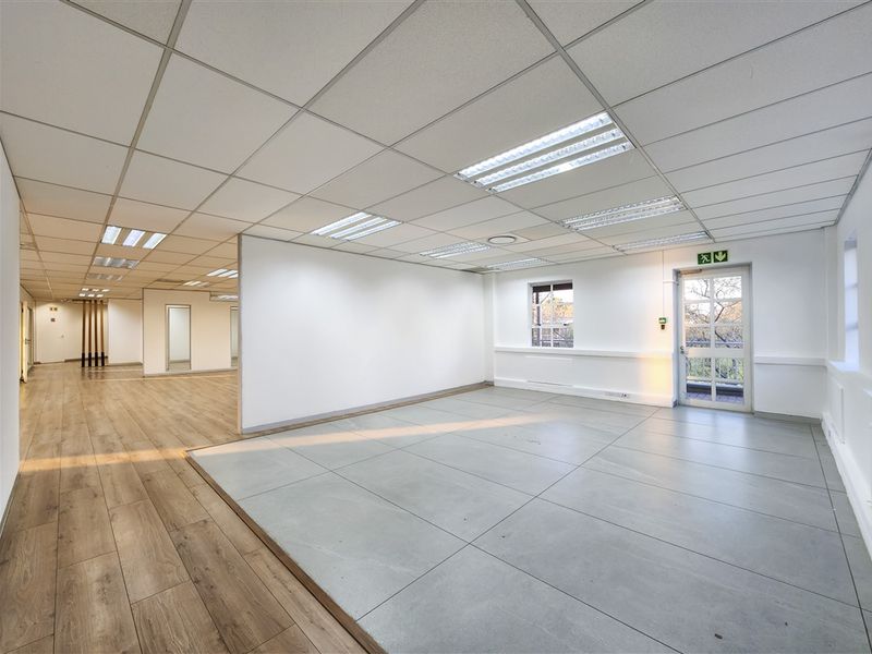 Spacious open-plan office area featuring a mix of laminate and tiled flooring, suspended ceilings with recessed lighting, and direct access to an external balcony.
