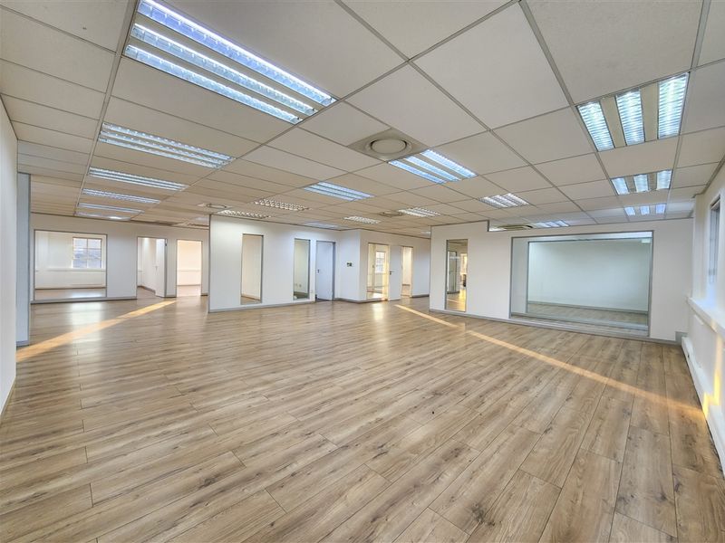Spacious open-plan office area featuring modern laminate flooring, suspended ceilings with recessed lighting, and glass-partitioned rooms for a bright, professional workspace.