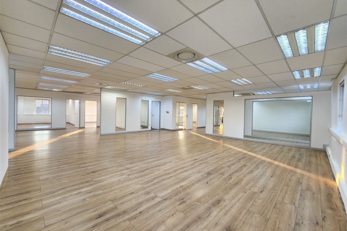Spacious open-plan office area featuring modern laminate flooring, suspended ceilings with recessed lighting, and glass-partitioned rooms for a bright, professional workspace.