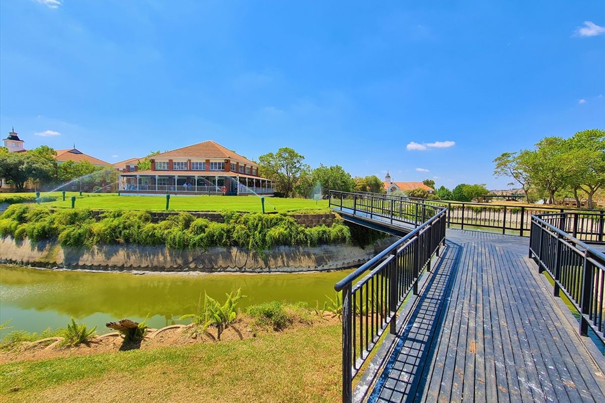 A scenic view of the office property grounds featuring a pedestrian bridge crossing a water feature towards the main building and landscaped lawns.