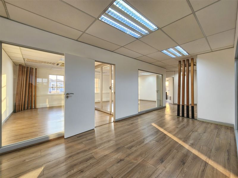 Modern office space featuring laminate flooring, glass partitions, and suspended ceilings with recessed lighting, offering a bright and professional open-plan work environment.