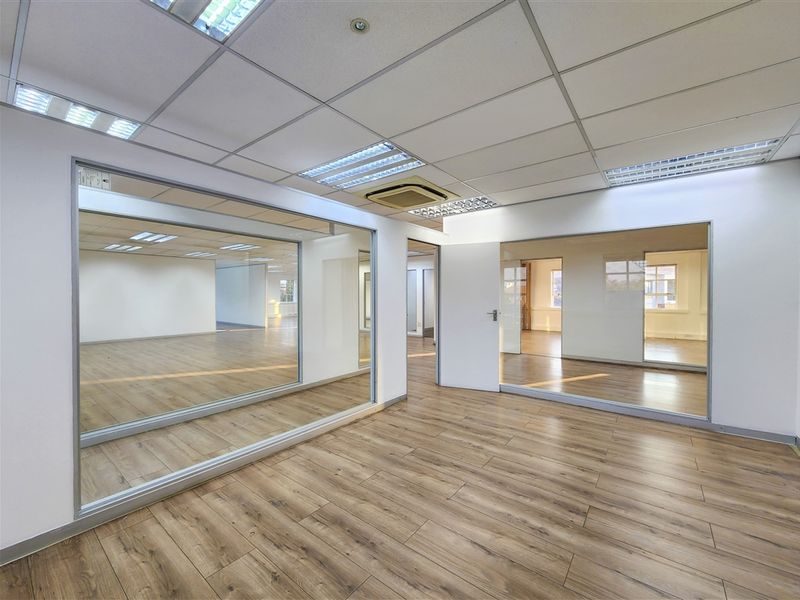 A bright, modern office space featuring laminate flooring, glass partitions, and a suspended ceiling with integrated lighting and air conditioning.