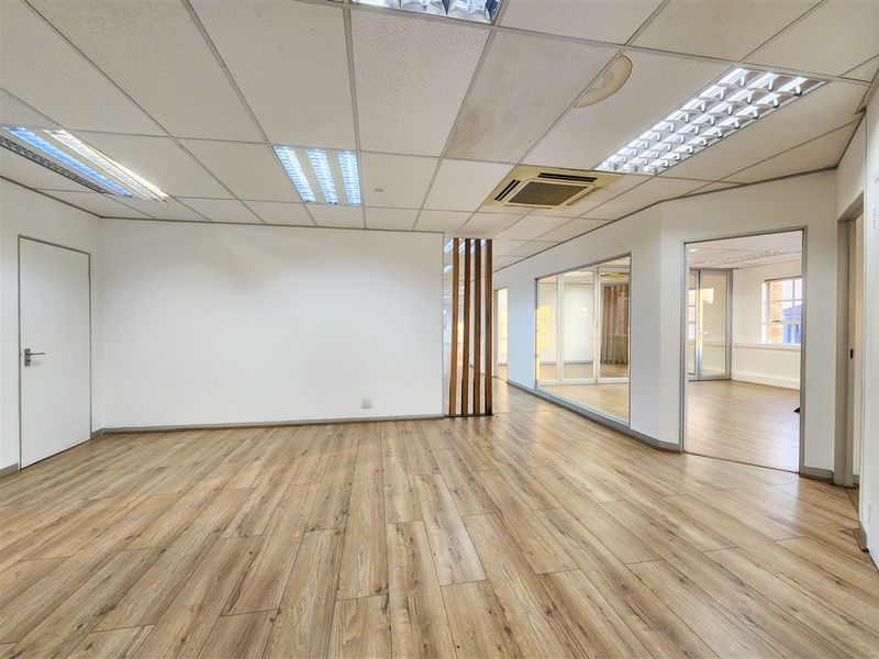 An open-plan office space featuring laminate flooring, glass partitions, and a suspended ceiling with integrated lighting and air conditioning.