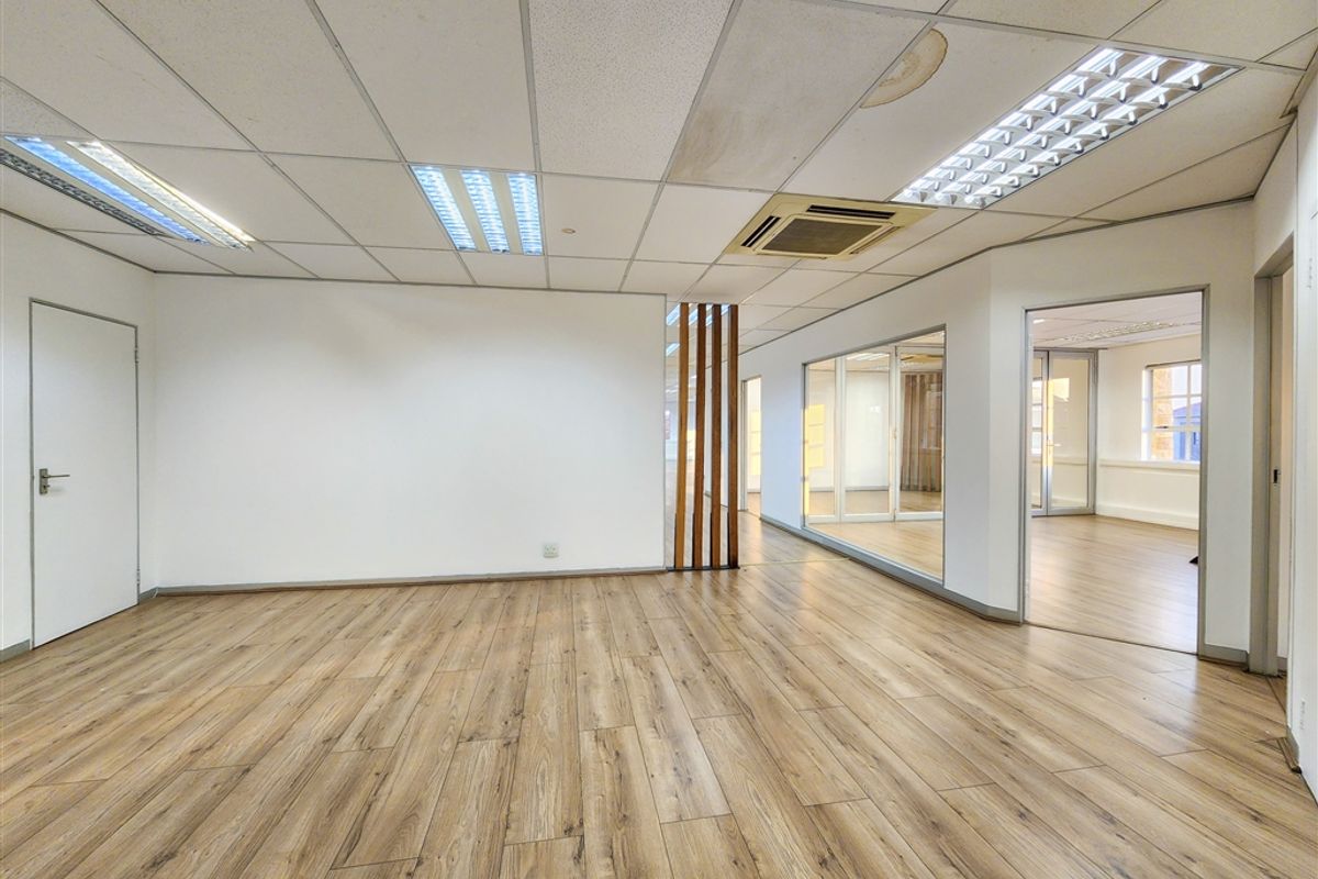 An open-plan office space featuring laminate flooring, glass partitions, and a suspended ceiling with integrated lighting and air conditioning.