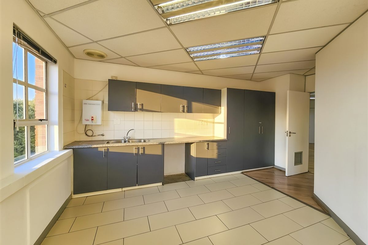 A functional office kitchenette featuring dark grey cabinetry, laminate countertops, a stainless steel sink, and tiled flooring under a suspended ceiling.