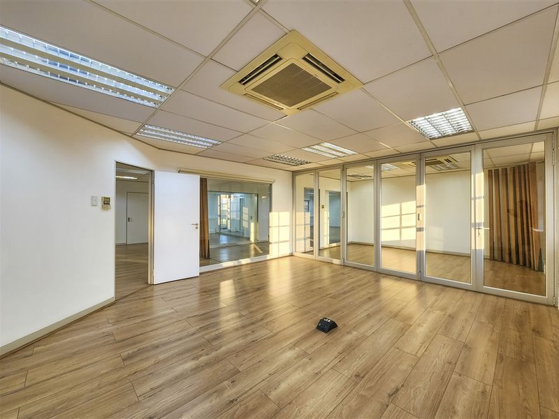 A bright, vacant office space featuring modern laminate flooring, glass partitions, and a suspended ceiling with integrated air conditioning and lighting.