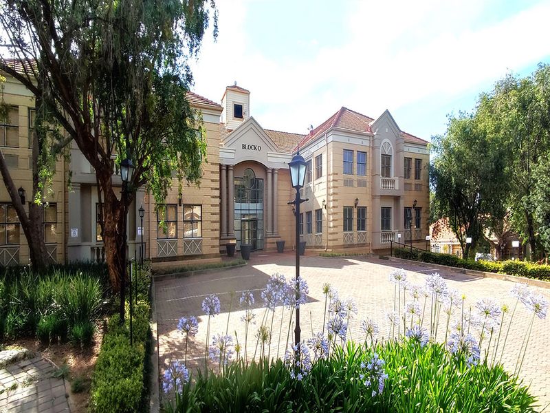 Front elevation of Block D office building featuring a paved driveway, classic architectural facade, and landscaped garden surroundings.