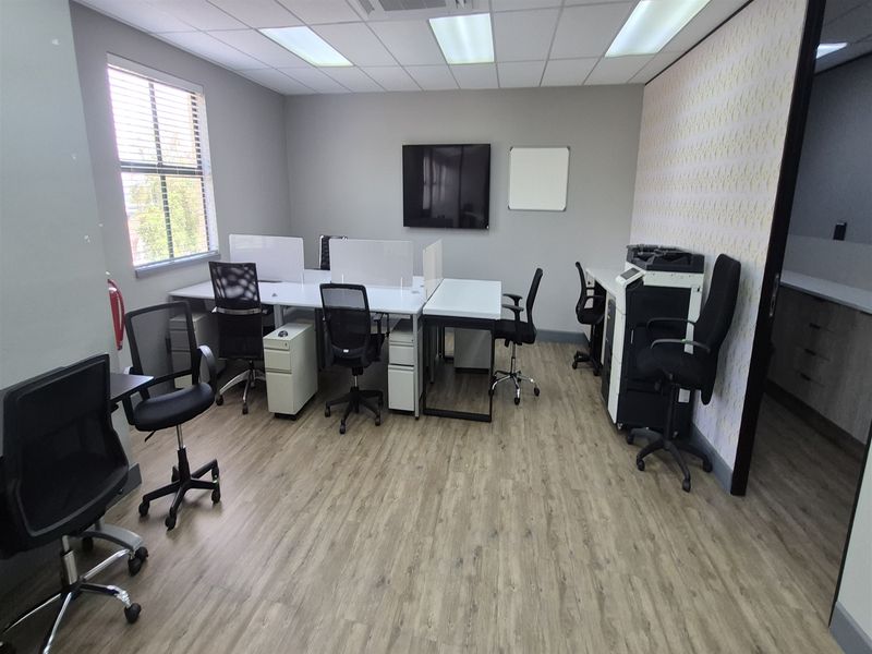 A functional office space featuring laminate flooring, a suspended ceiling with recessed lighting, and a decorative feature wall.