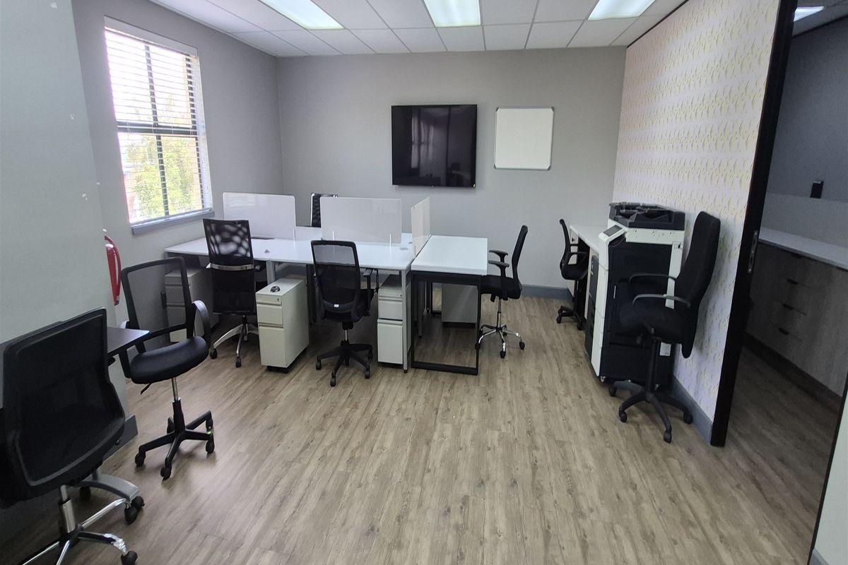 A functional office space featuring laminate flooring, a suspended ceiling with recessed lighting, and a decorative feature wall.
