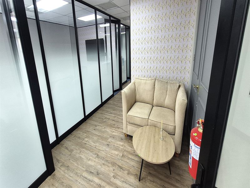 A modern office space featuring glass partition walls, wood-look laminate flooring, and a suspended ceiling with recessed lighting.