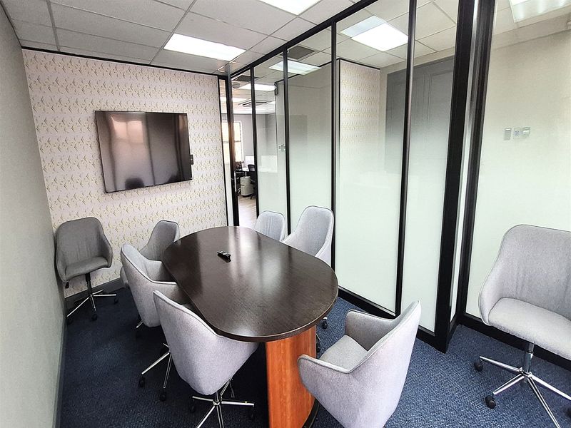 A professional office meeting room featuring a glass partition wall, suspended ceiling with recessed lighting, and carpeted flooring.