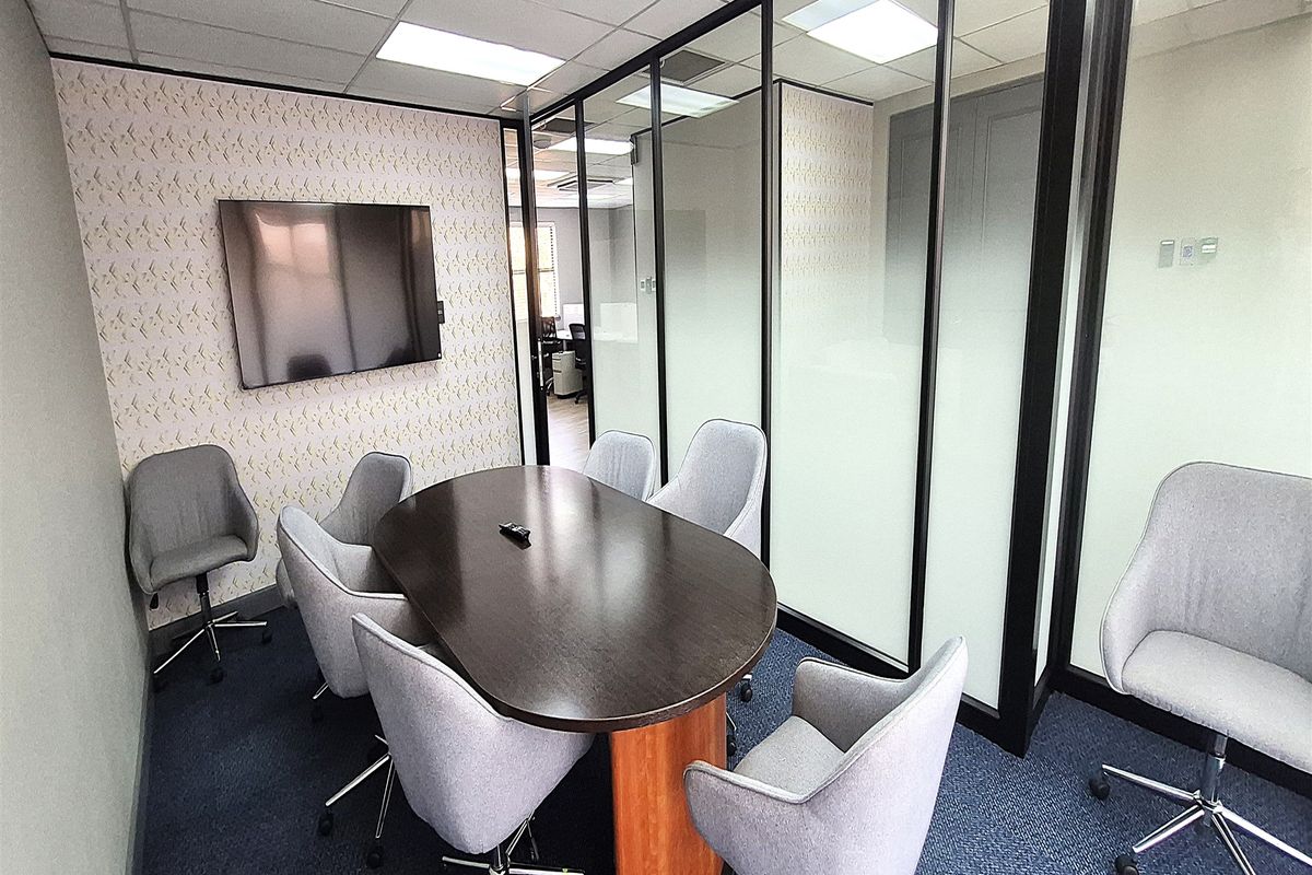 A professional office meeting room featuring a glass partition wall, suspended ceiling with recessed lighting, and carpeted flooring.