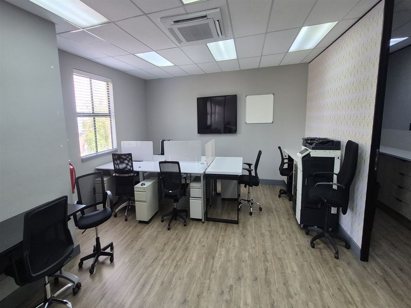 A well-maintained office space featuring laminate flooring, a suspended ceiling with recessed lighting, and a ceiling-mounted air conditioning unit.