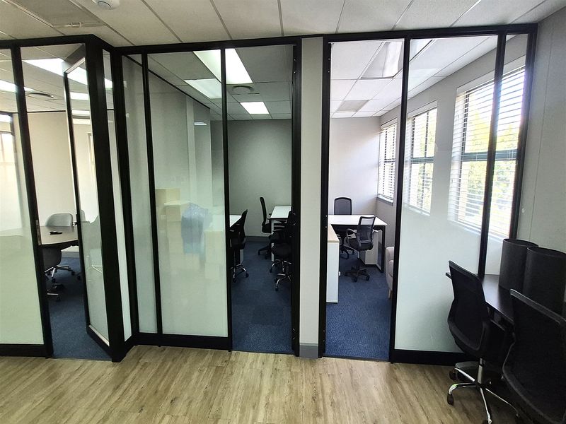 Modern office space featuring glass partition walls, suspended ceilings with recessed lighting, and a combination of carpet and laminate flooring.