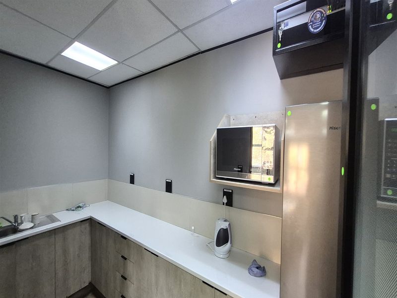 A modern office kitchenette featuring sleek cabinetry, a clean laminate countertop, stainless steel sink, and integrated microwave shelf.