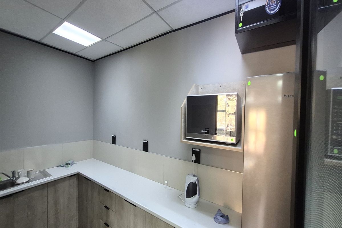 A modern office kitchenette featuring sleek cabinetry, a clean laminate countertop, stainless steel sink, and integrated microwave shelf.