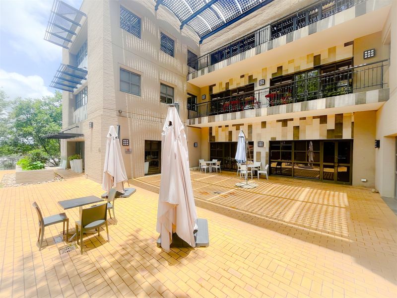 A spacious multi-level outdoor courtyard and patio area featuring paved flooring, metal railings, and overhead pergola shading, suitable for office break-out or social use.