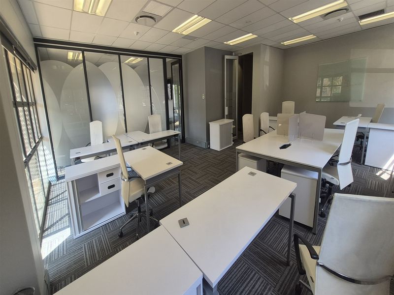 A professional office space featuring a suspended ceiling, recessed lighting, glass partitioning, and modern carpet tiles, providing a clean and functional work environment.
