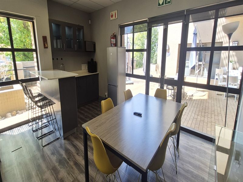 Modern open-plan office kitchenette and dining area featuring laminate flooring, built-in cabinetry, and large glass doors leading to an outdoor patio.
