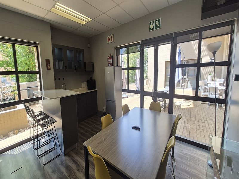 Open-plan office kitchenette and dining area featuring modern cabinetry, laminate flooring, and large glass doors providing direct access to an outdoor patio space.