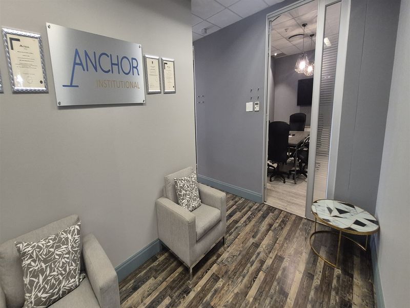 Professional office reception area featuring modern laminate flooring, a glass partition door leading to a meeting room, and contemporary wall-mounted signage.