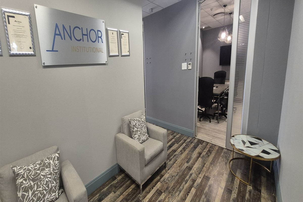 Professional office reception area featuring modern laminate flooring, a glass partition door leading to a meeting room, and contemporary wall-mounted signage.