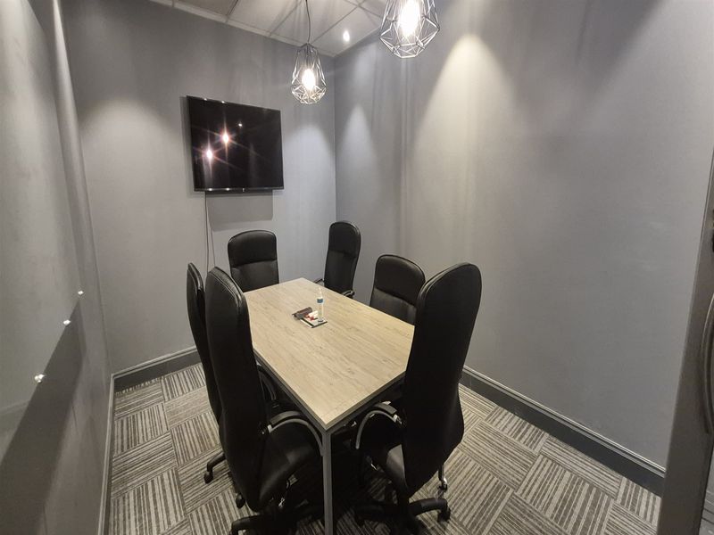 A compact, modern office meeting room featuring grey walls, carpet tiles, and contemporary pendant lighting, suitable for professional collaboration.