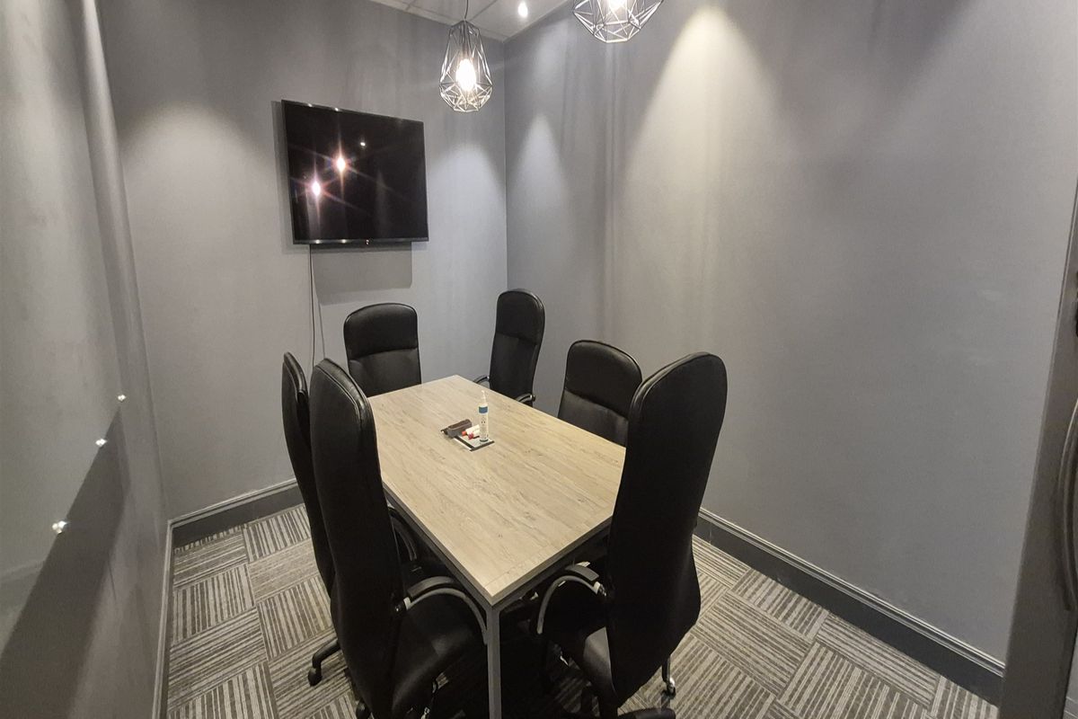 A compact, modern office meeting room featuring grey walls, carpet tiles, and contemporary pendant lighting, suitable for professional collaboration.