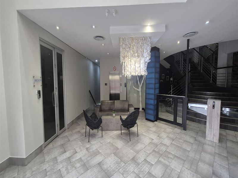 Modern office building lobby featuring a tiled floor, elevator access, and a feature staircase with contemporary lighting.