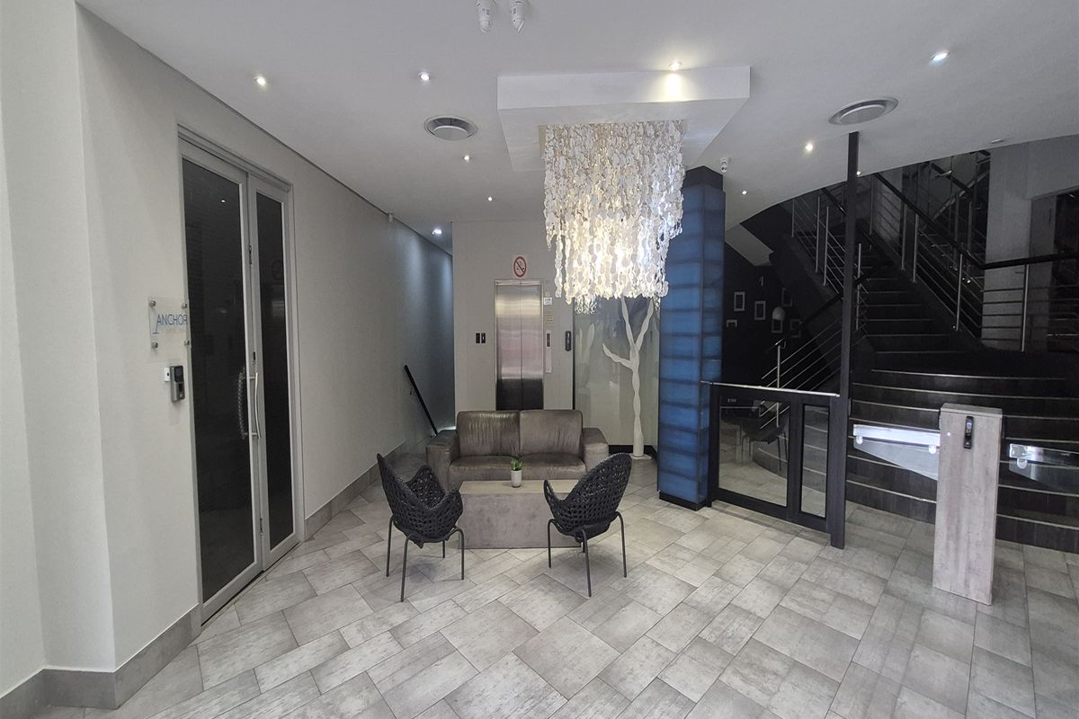 Modern office building lobby featuring a tiled floor, elevator access, and a feature staircase with contemporary lighting.