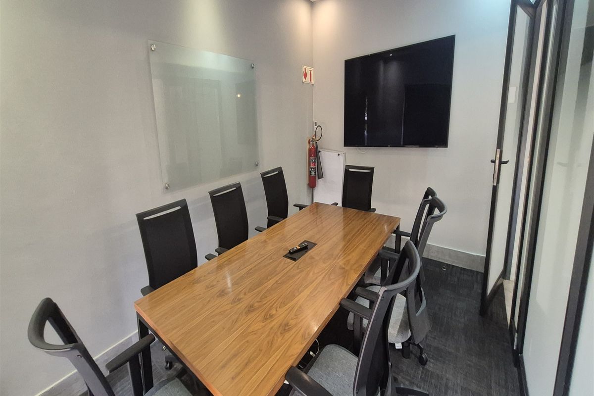 A professional meeting room featuring a wooden conference table, glass whiteboard, wall-mounted display, and modern glass partition entry.