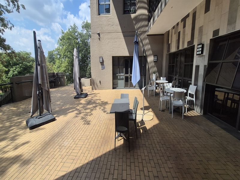 A spacious outdoor patio area featuring brick paving, wall-mounted lighting, and direct access to the office building through glass-paneled doors.