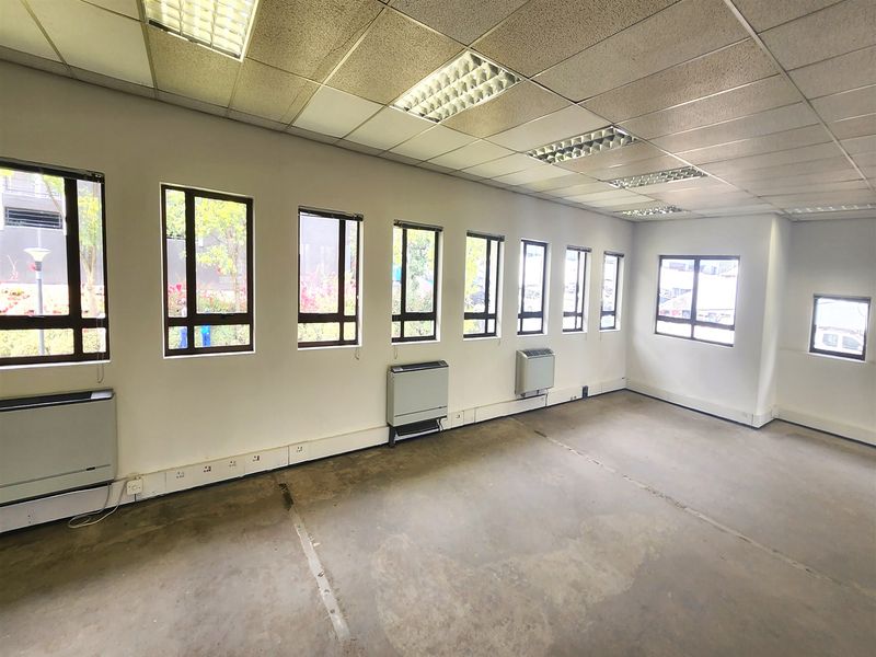 An empty office space featuring a suspended ceiling, recessed lighting, wall-mounted HVAC units, and multiple windows with perimeter electrical trunking.