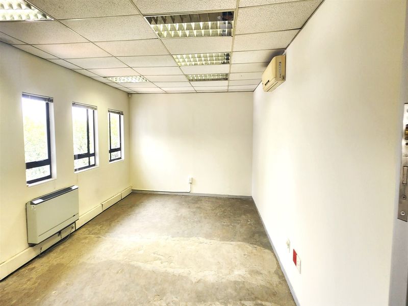 An empty office space featuring a suspended ceiling, recessed lighting, wall-mounted air conditioning, and a wall-mounted heater with concrete flooring.