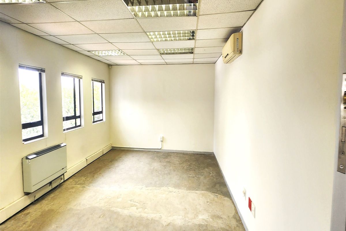 An empty office space featuring a suspended ceiling, recessed lighting, wall-mounted air conditioning, and a wall-mounted heater with concrete flooring.