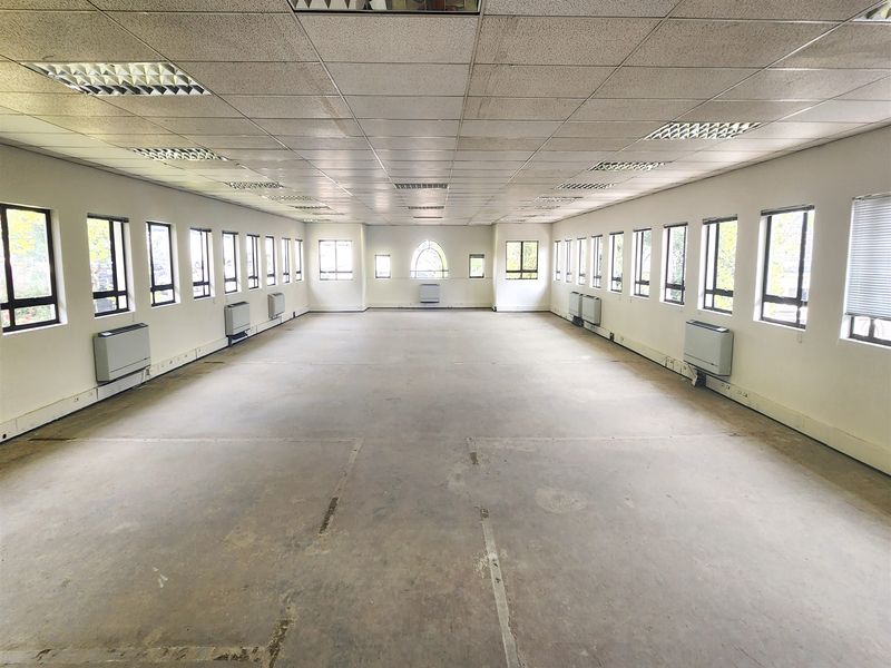A large, vacant open-plan office space featuring a suspended ceiling, recessed lighting, and multiple wall-mounted HVAC units along the perimeter.