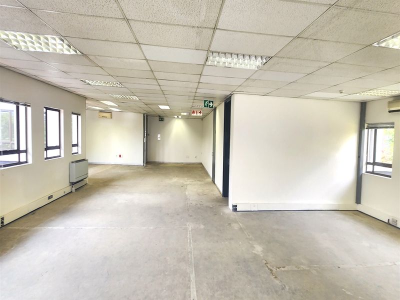 An open-plan office space featuring a suspended ceiling, recessed lighting, split-system air conditioning, and large windows, currently in a vacant shell condition.