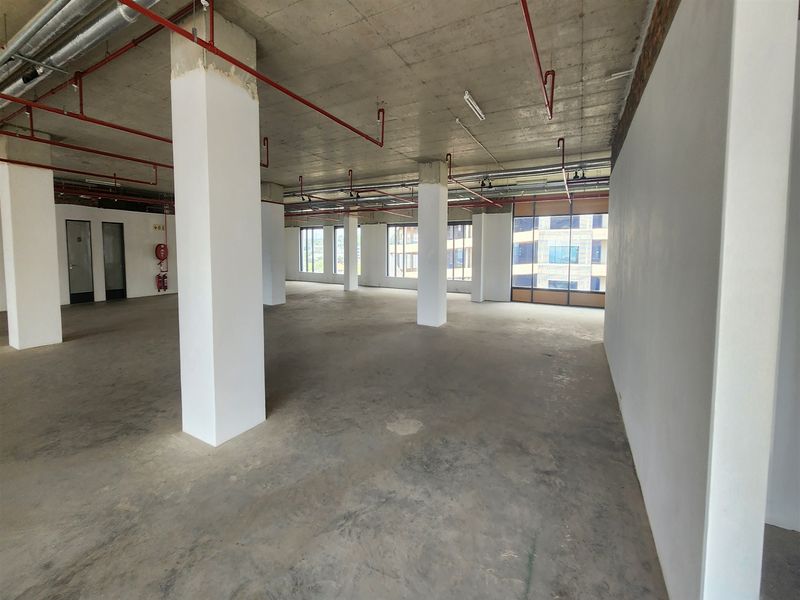An expansive, open-plan office space featuring an industrial aesthetic with exposed concrete ceilings, structural columns, and large windows providing ample natural light.