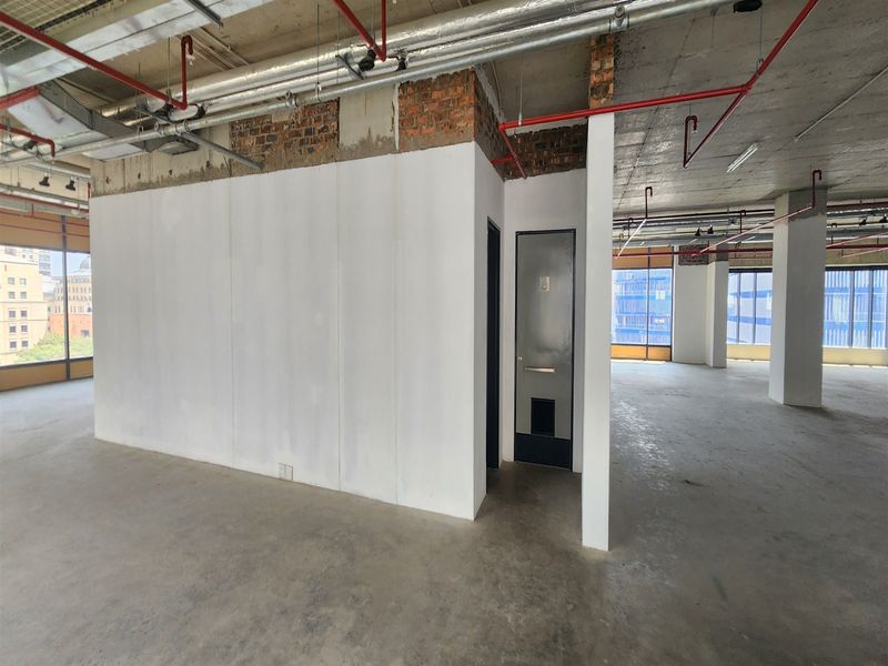 Open-plan office space in shell condition featuring exposed industrial ceilings, concrete flooring, and large windows providing ample natural light.